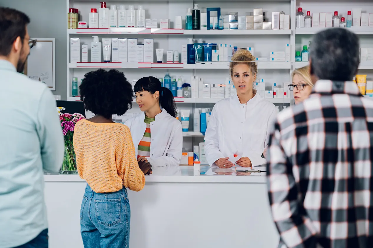 Woman pharmacist smiling in a pharmacy, surrounded by shelves of medicines, showcasing healthcare professionalism.